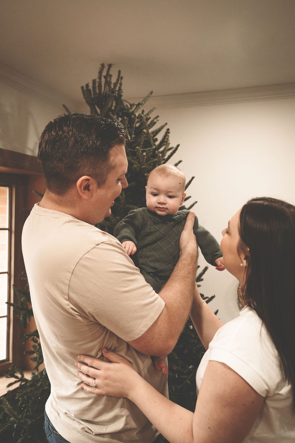 A couple dances together in a dimly lit room with a Christmas tree in the background.