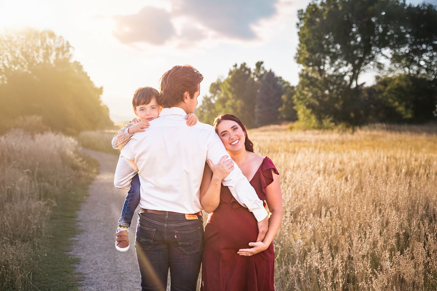 Denver maternity photography session with a couple and their young son at golden hour in an open field of tall grass.