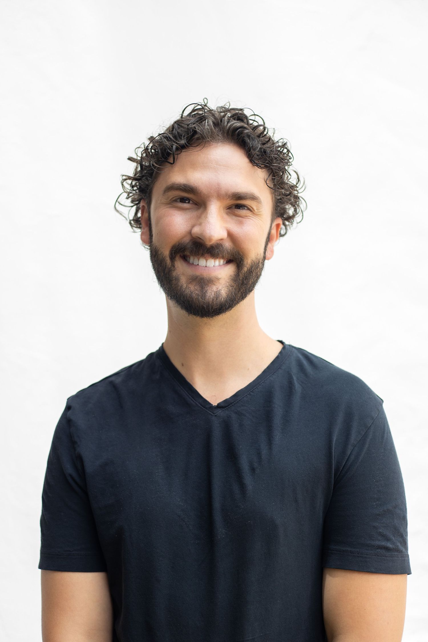 A person in a black v-neck t-shirt smiles against a white background.