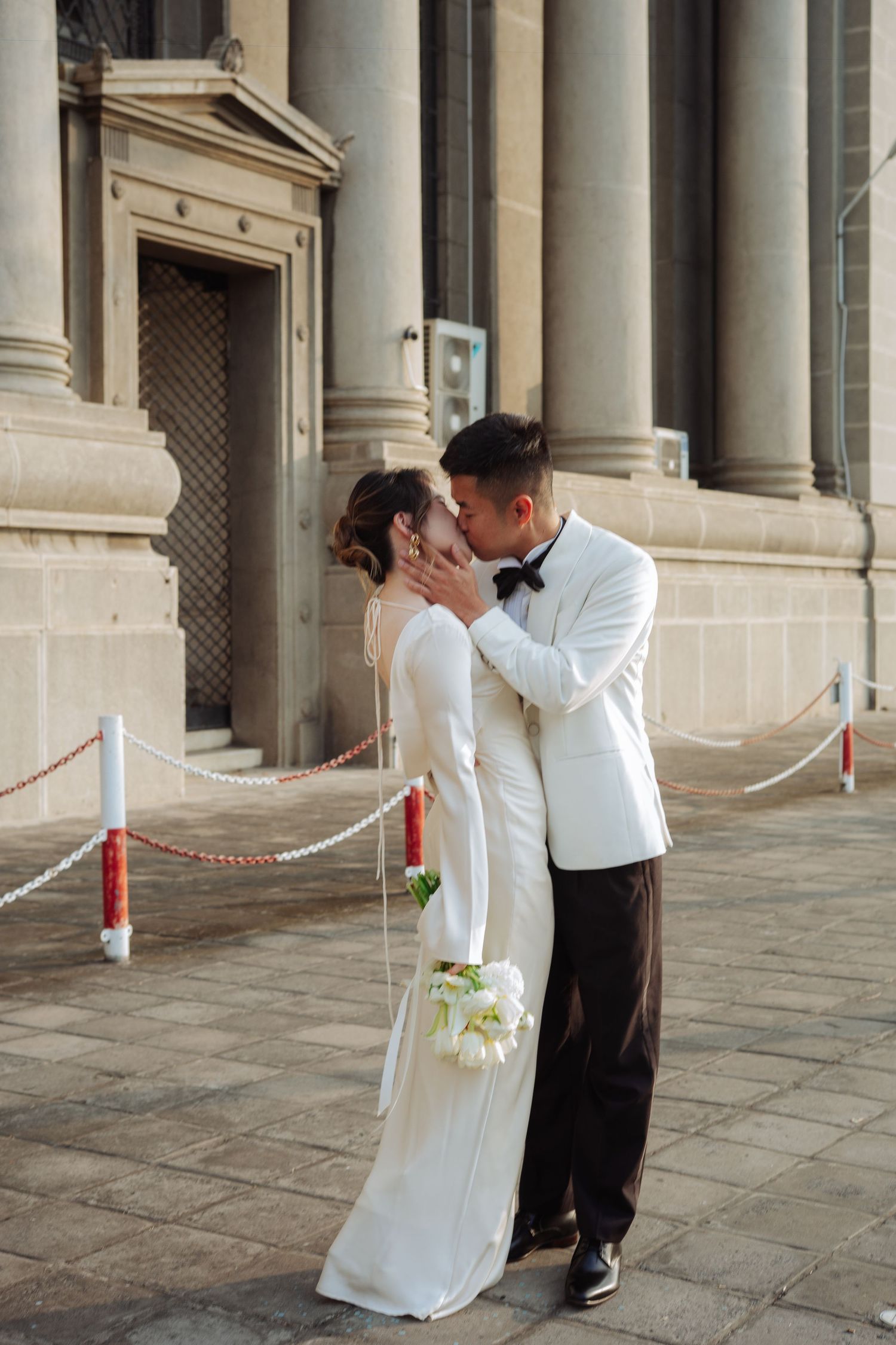 Bride and groom share a kiss in front of grand stone columns outdoors.