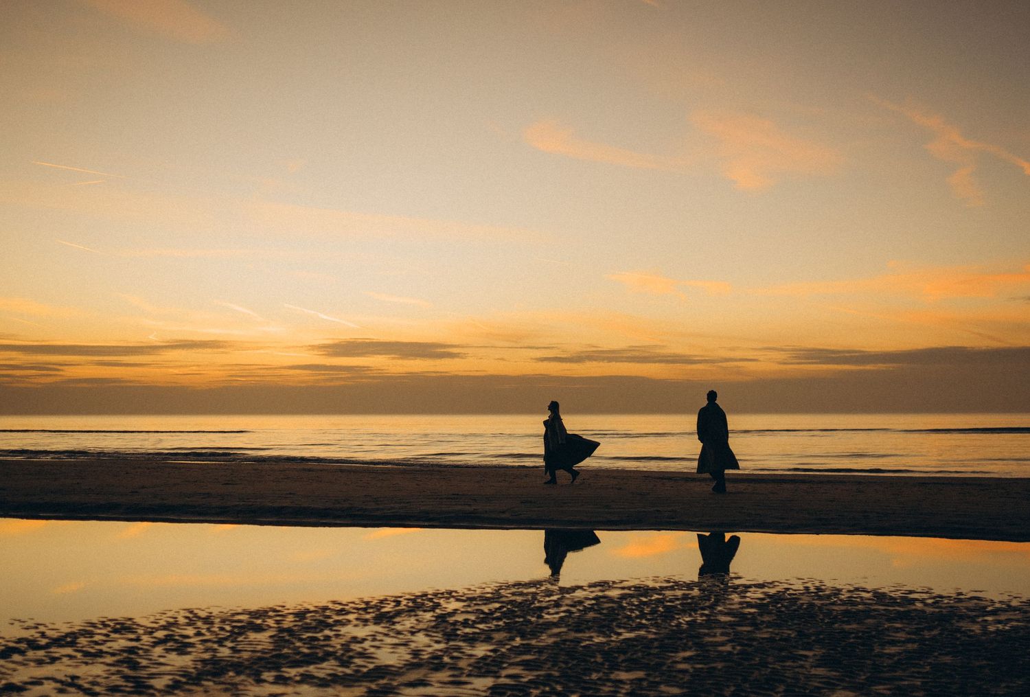 Silhouettes of figures walking along a beach at sunset with dramatic orange sky.