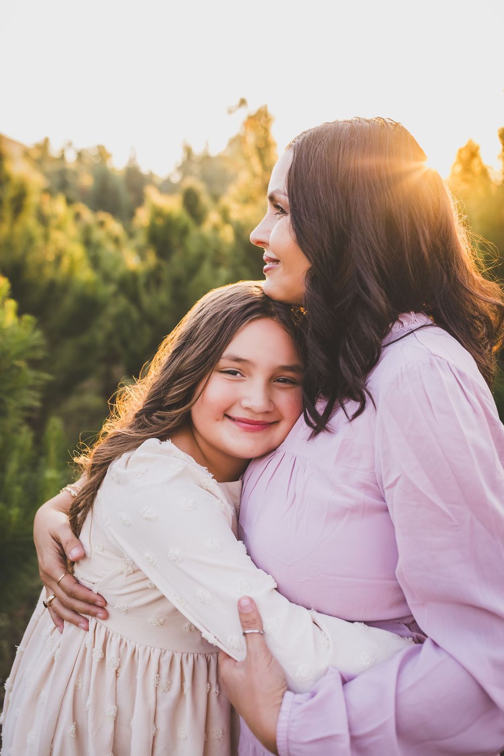 Two people in pink and white outfits embrace during a sunset photoshoot in a wooded outdoor setting.