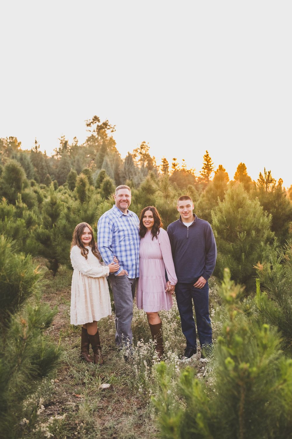 A group stands together at sunset among evergreen trees during a golden hour outdoor photo session.