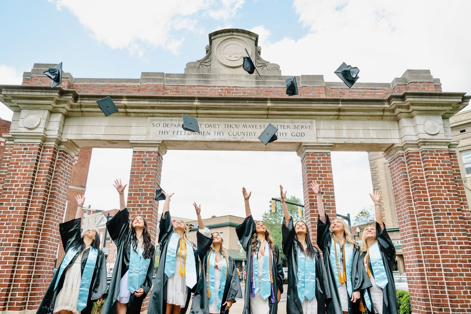Graduates in blue caps and gowns throw their mortarboards into the air during commencement ceremony celebration.