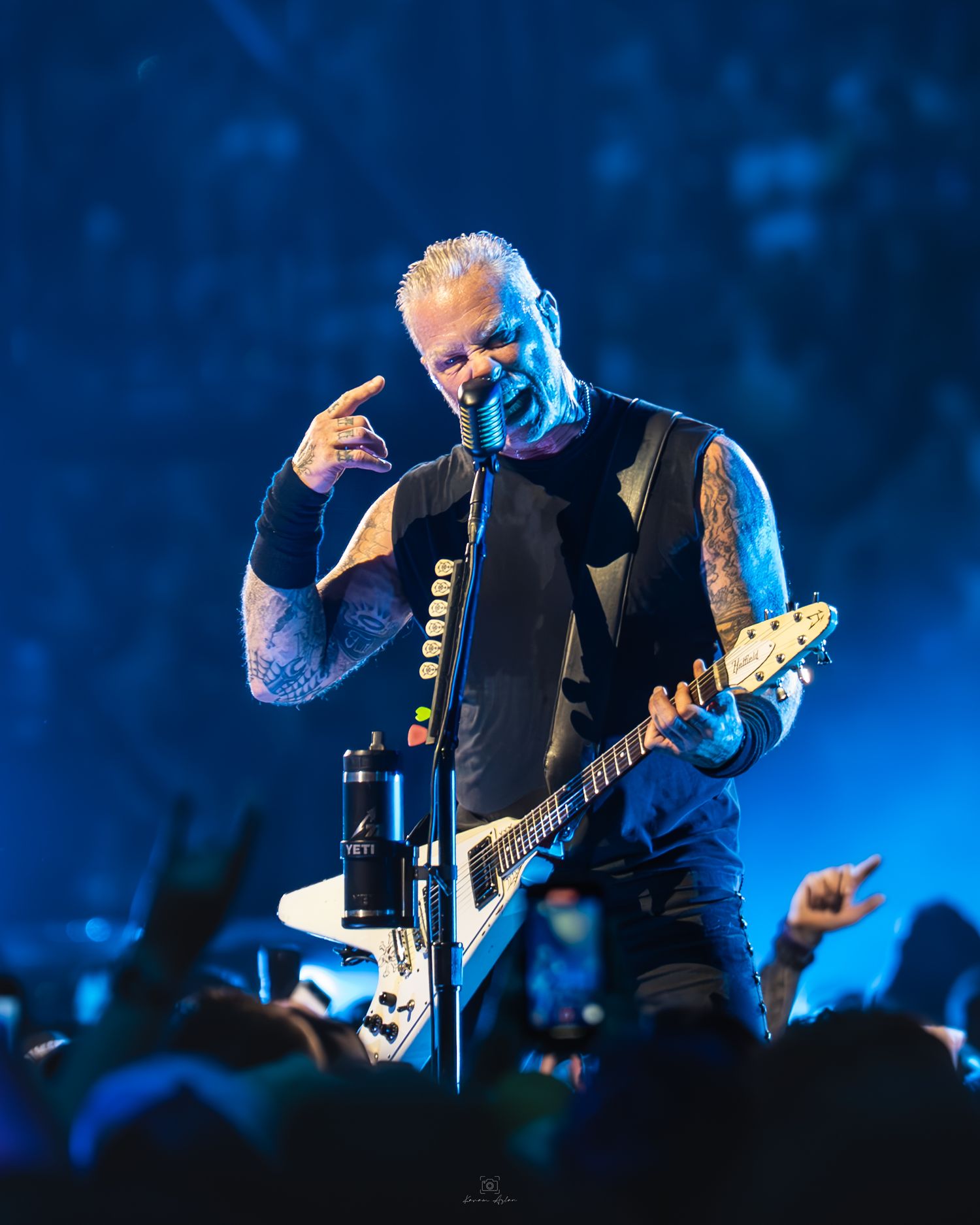 A musician performs on stage with an electric guitar under dramatic blue lighting during a concert performance.