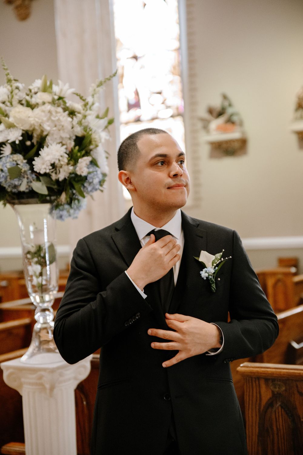 Groom in black suit adjusting his tie in church before the ceremony.