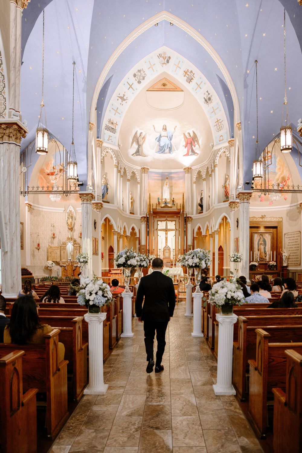 A person walks down the aisle of an ornate Catholic church decorated with white flowers and gothic arches.