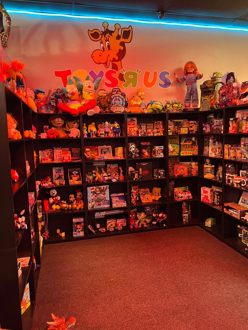 Vintage toy store display room with red carpeting, neon lighting, and shelves of collectible items.