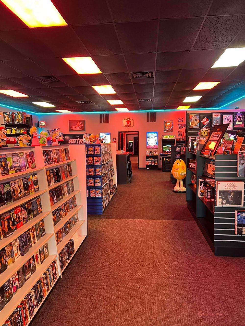 Long aisle of a retro gaming store with rows of display shelves and orange accents.