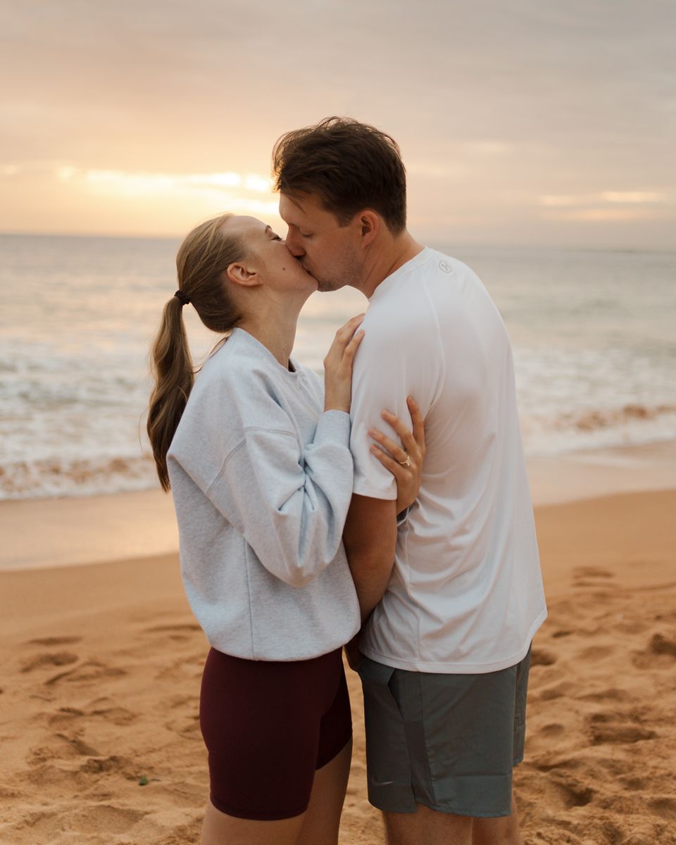 A couple hugging and kissing at Newport beach, dressed in white and casual attire during an engagement photoshoot in sydney