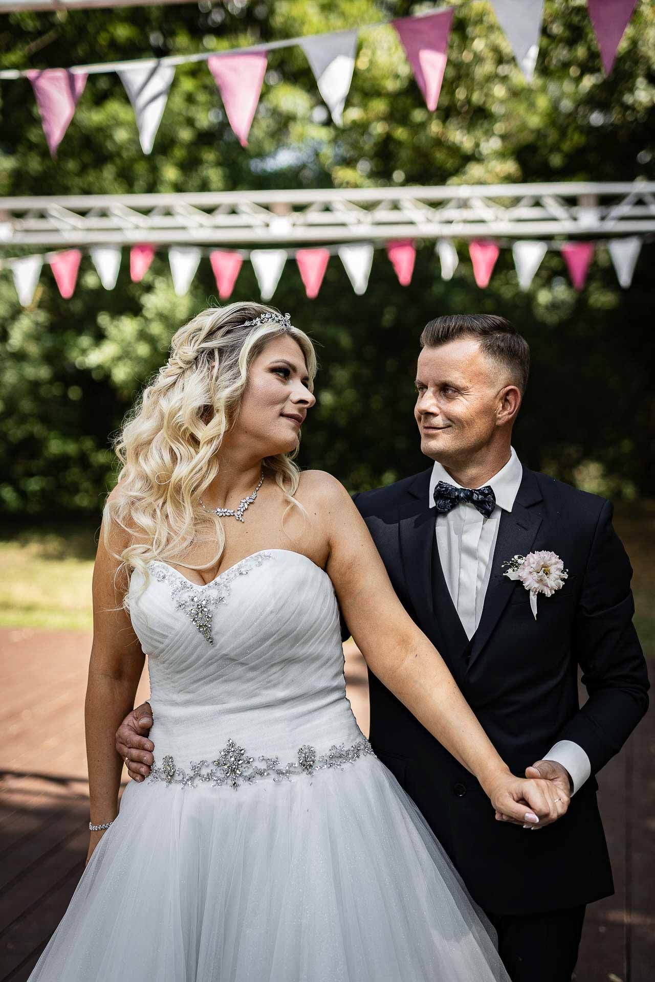 Wedding couple poses under pink bunting decorations at their outdoor reception.