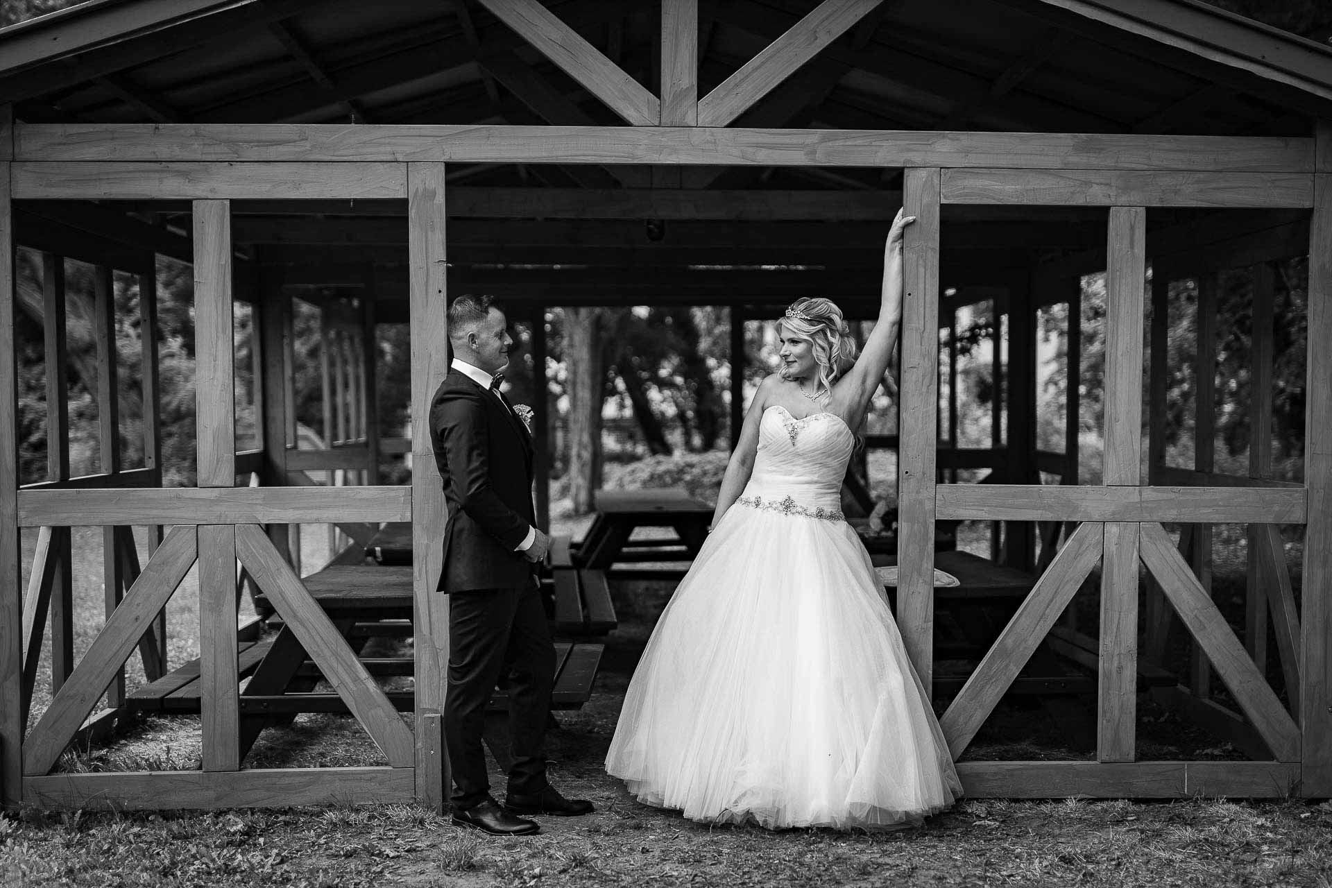 Black and white wedding portraits taken under a rustic wooden pavilion structure.