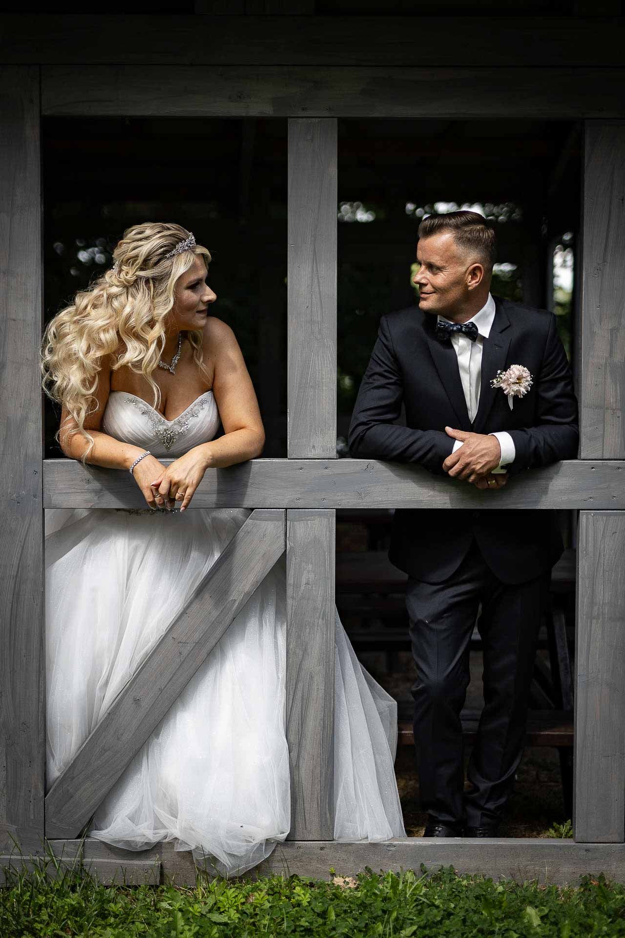 Artistic wedding portraits through wooden fence panels create unique framing effect.