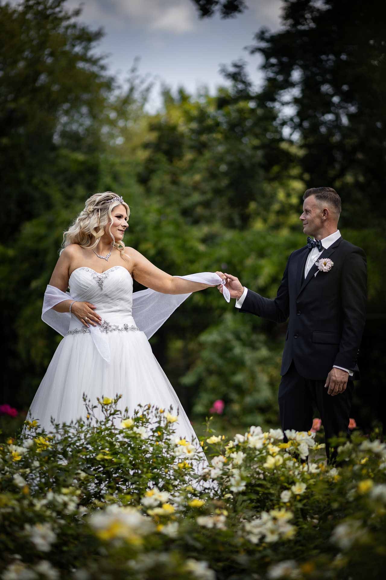 Wedding couple poses playfully among blooming garden flowers on their special day.