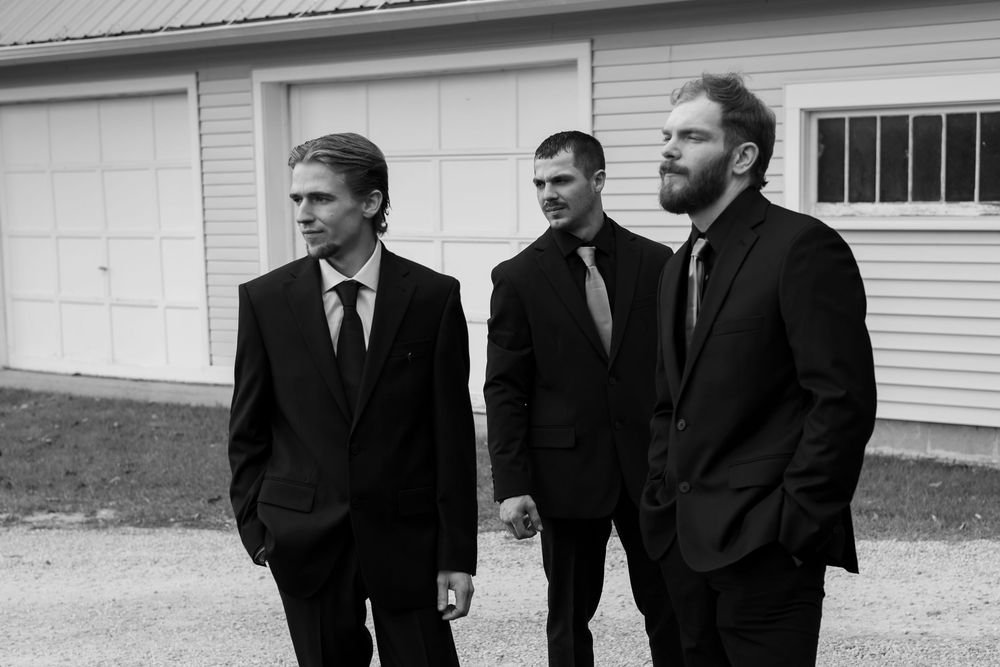 A group of people in dark coats stand in a row against a white building exterior.