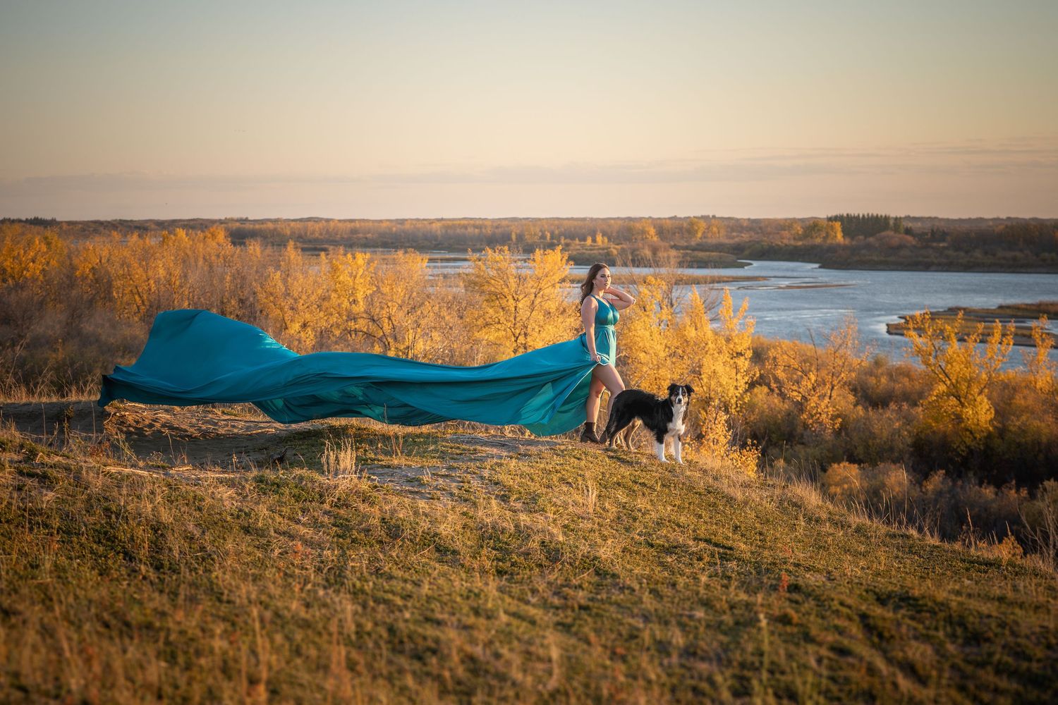 Scenic autumn landscape with golden trees and blue lake stretching across rolling hills at sunset.