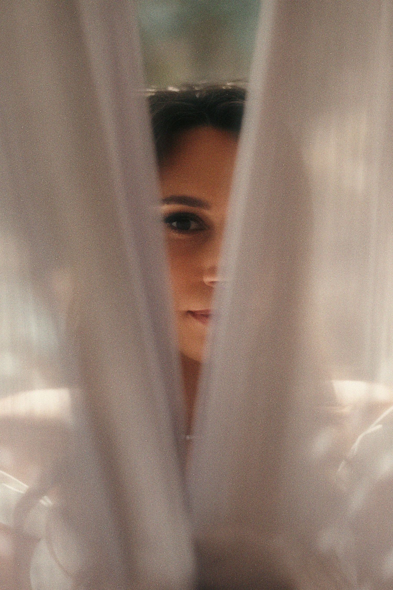 A mysterious figure is partially visible through sheer white curtains or fabric creating an ethereal veiled effect.