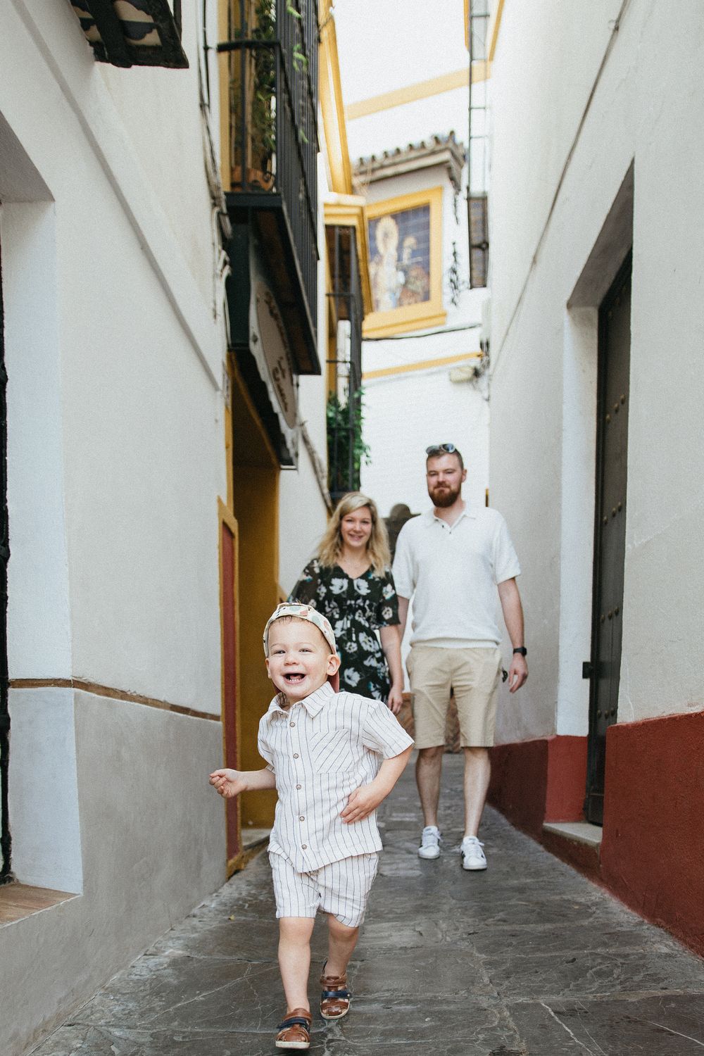 A family explores a narrow cobblestone alley in a historic Spanish neighborhood with white and yellow walls.