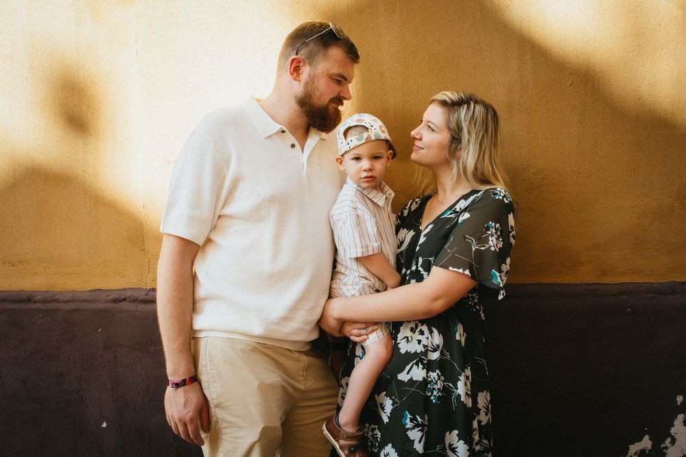 A family in coordinated outfits stands together against a warm-toned wall in a candid portrait.