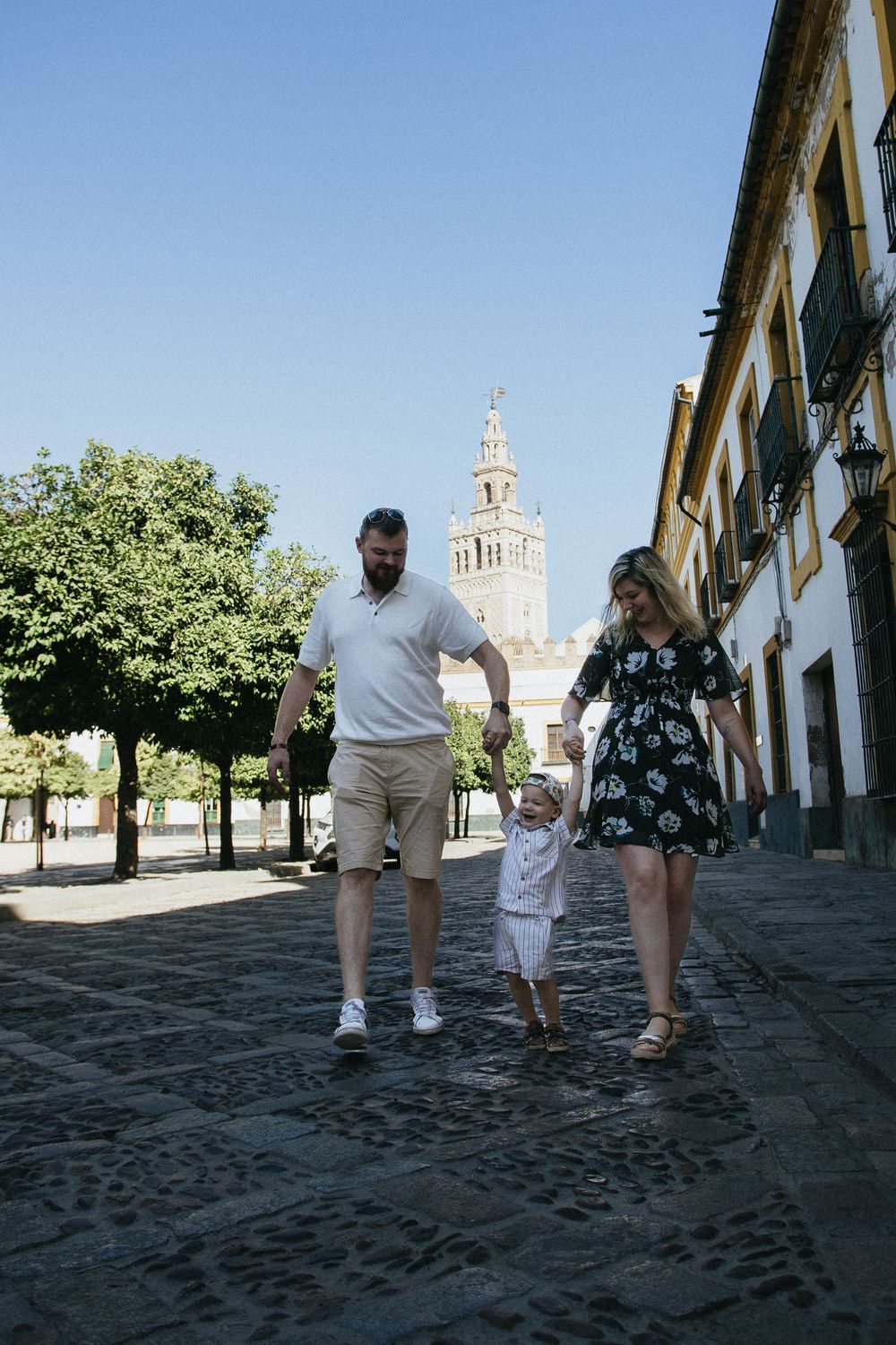 A cobblestone street with historic architecture and a church tower visible in the background.