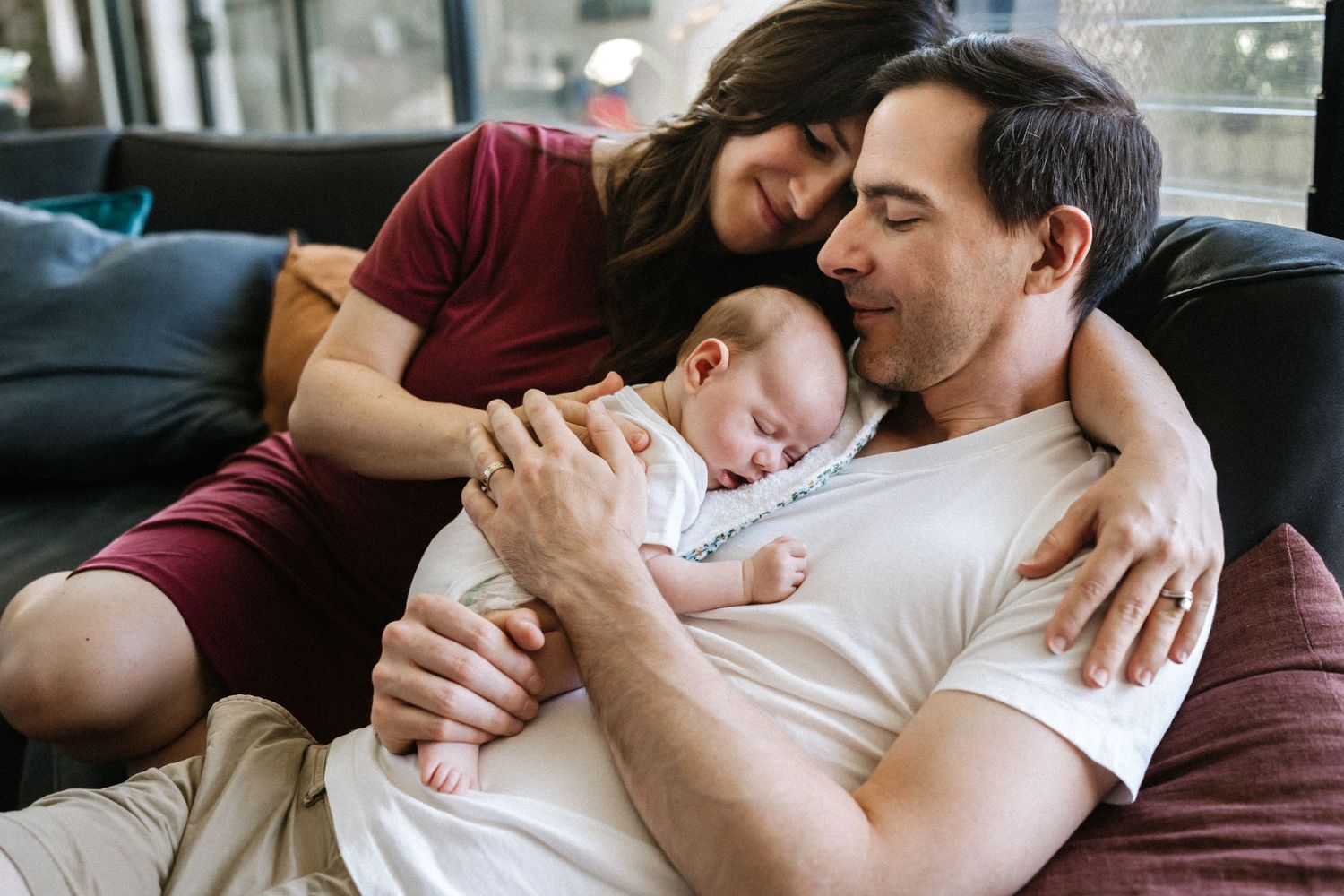 Mother and father on a couch holding their newborn baby during an indoor newborn photography session in Perth