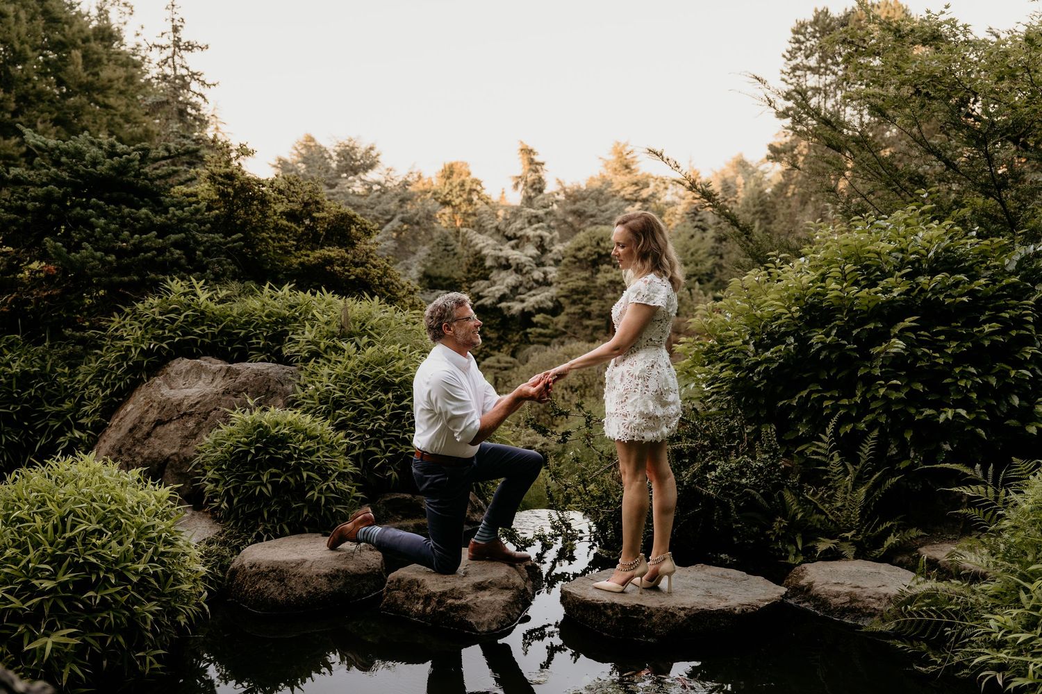 Man Proposing to woman on rocks over water in Kubota Garden