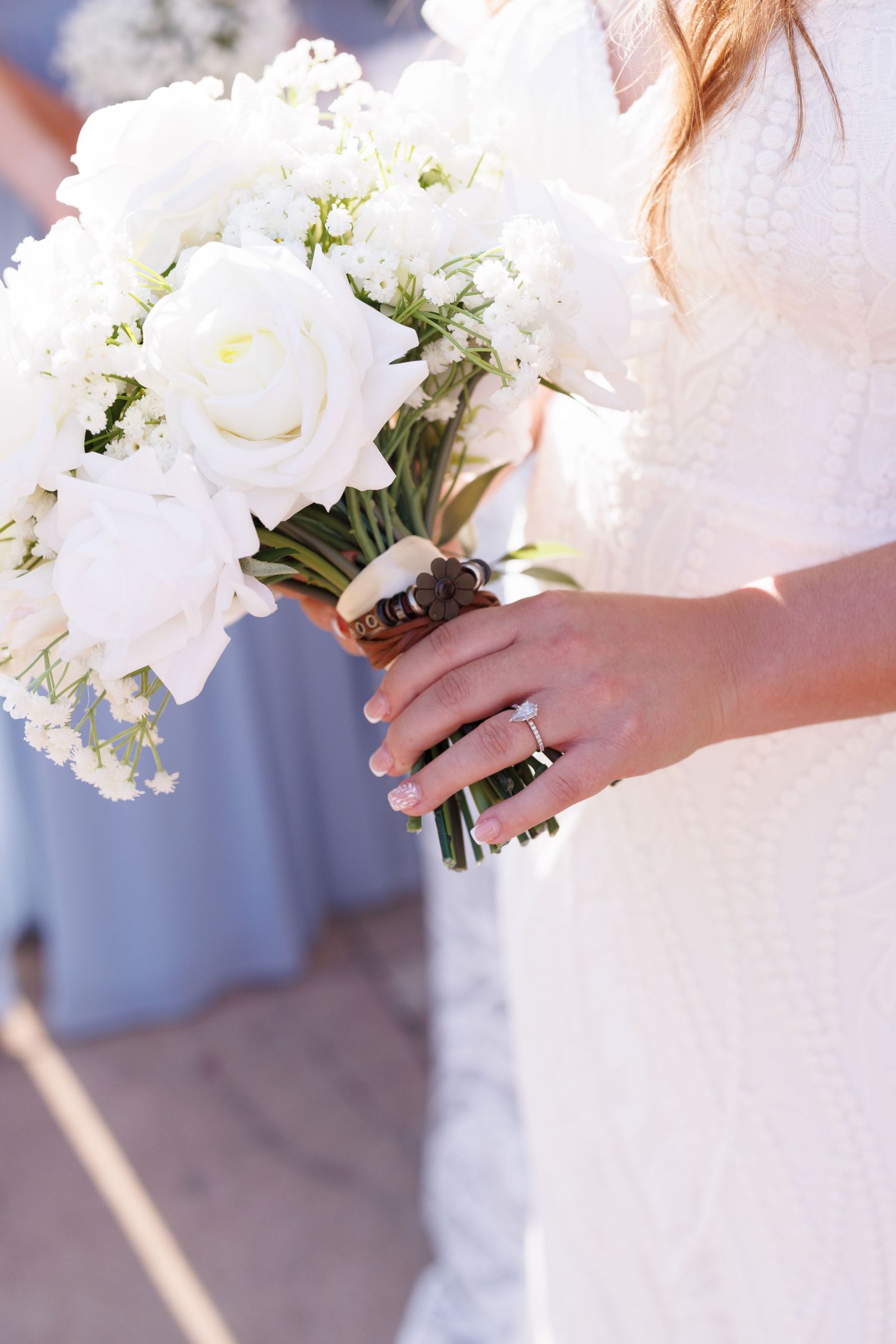 Close-up of a bridal bouquet with white roses and delicate flowers held by hands wearing a wedding ring.