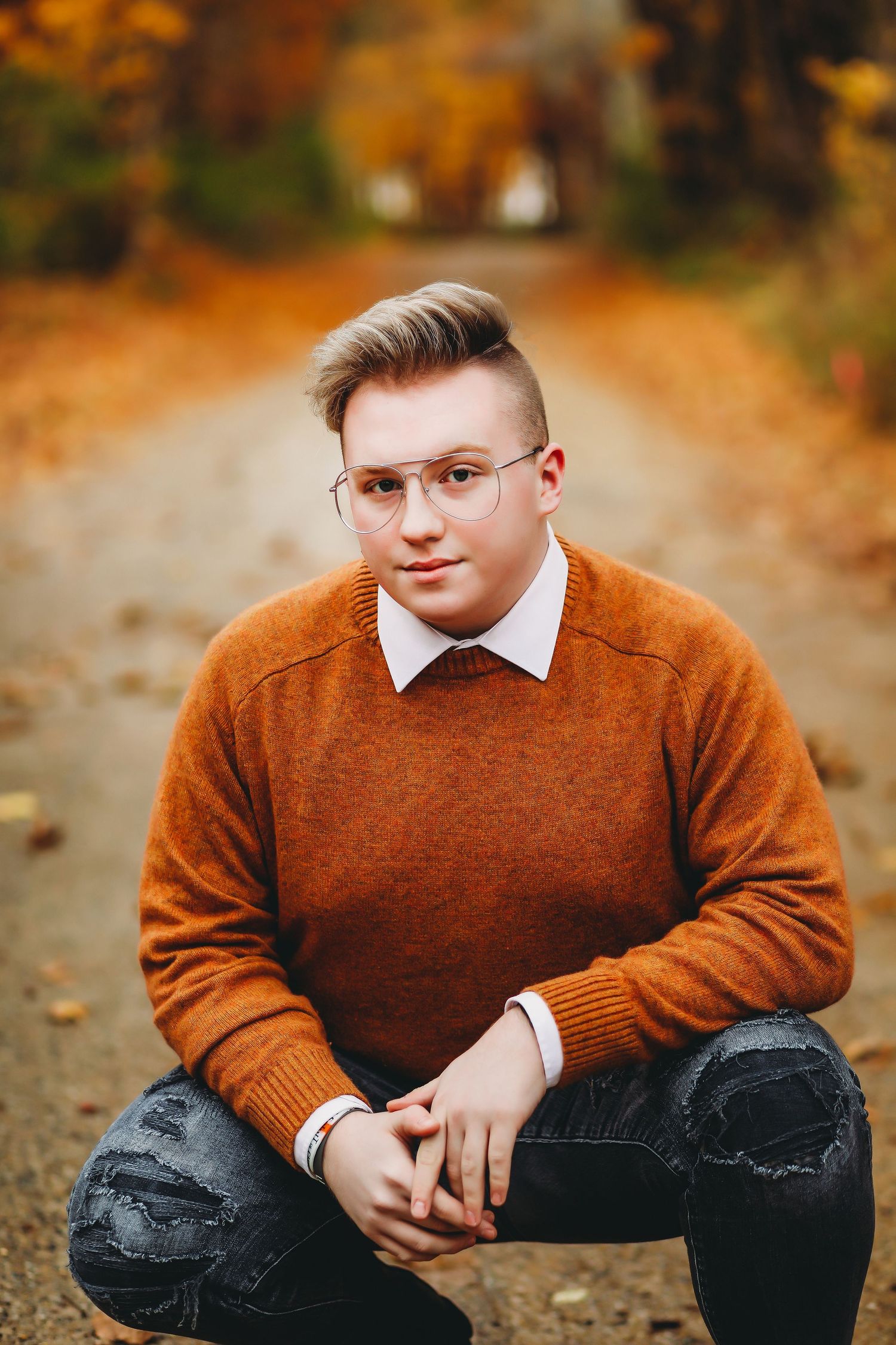 Person in orange sweater and glasses poses on autumn path with fallen leaves.
Best child's photographer in Illinois