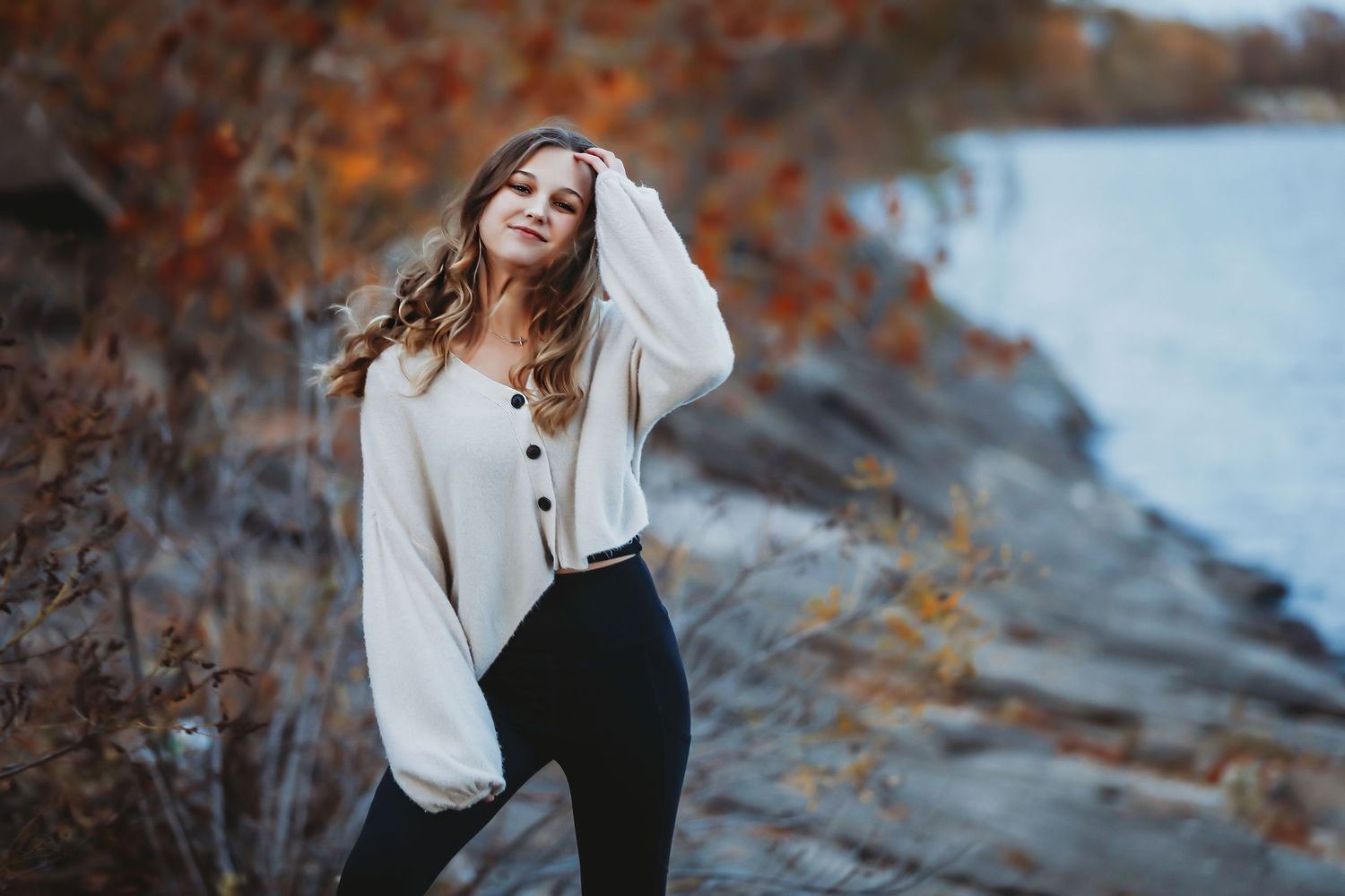 Woman in cream sweater poses against autumn foliage by waterfront at sunset.
Best teen's photographer in Illinois