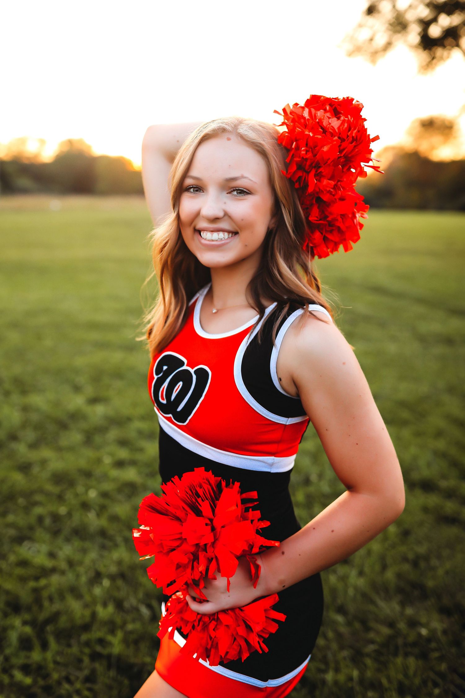 Cheerleader in red and black uniform with pom poms poses in grassy field at sunset.
Best teen photographer in Illinois