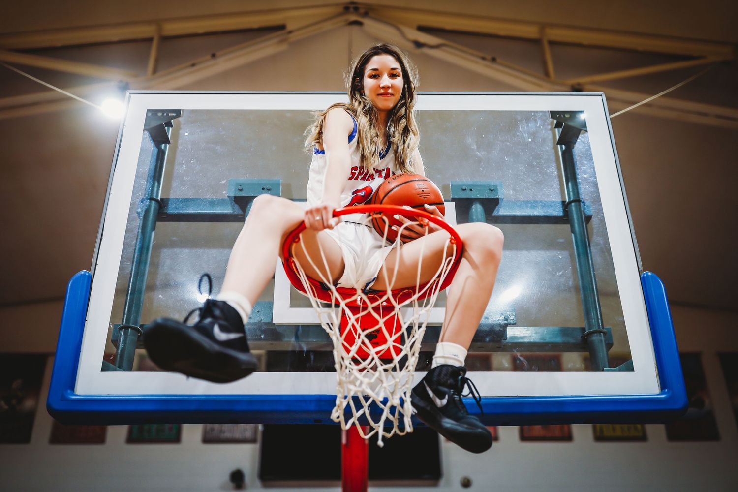 Athletic figure sitting on a basketball hoop in a red outfit against dramatic lighting in a gym.
Best teen's photographer in Illinois
