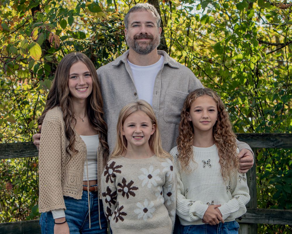 Casual family photo on wooden deck with natural greenery backdrop.