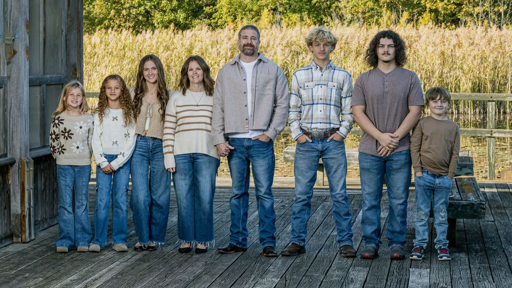 Wide shot of family members lined up on wooden deck with fall scenery.