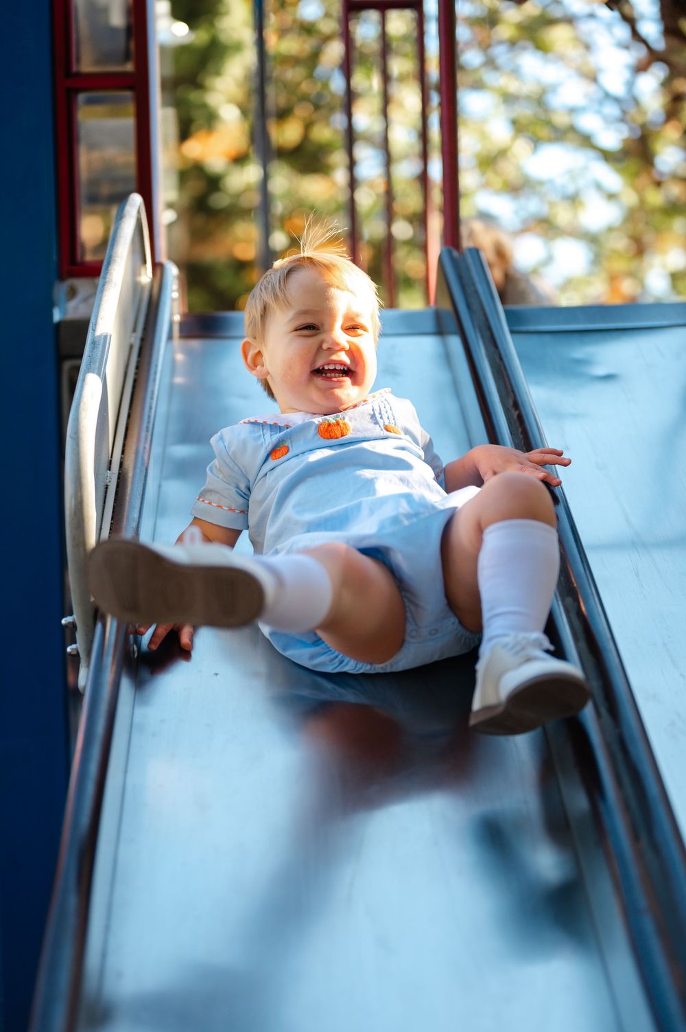 A sequence of photos shows a joyful baby sliding down a blue playground slide on a sunny day.