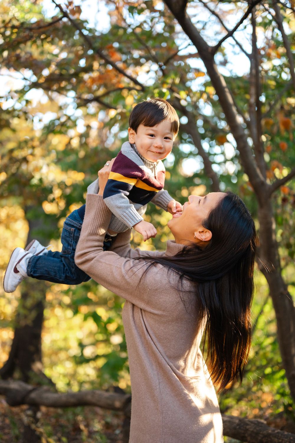 A parent and child share a joyful moment playing together outdoors on an autumn day with golden sunlight filtering through trees.