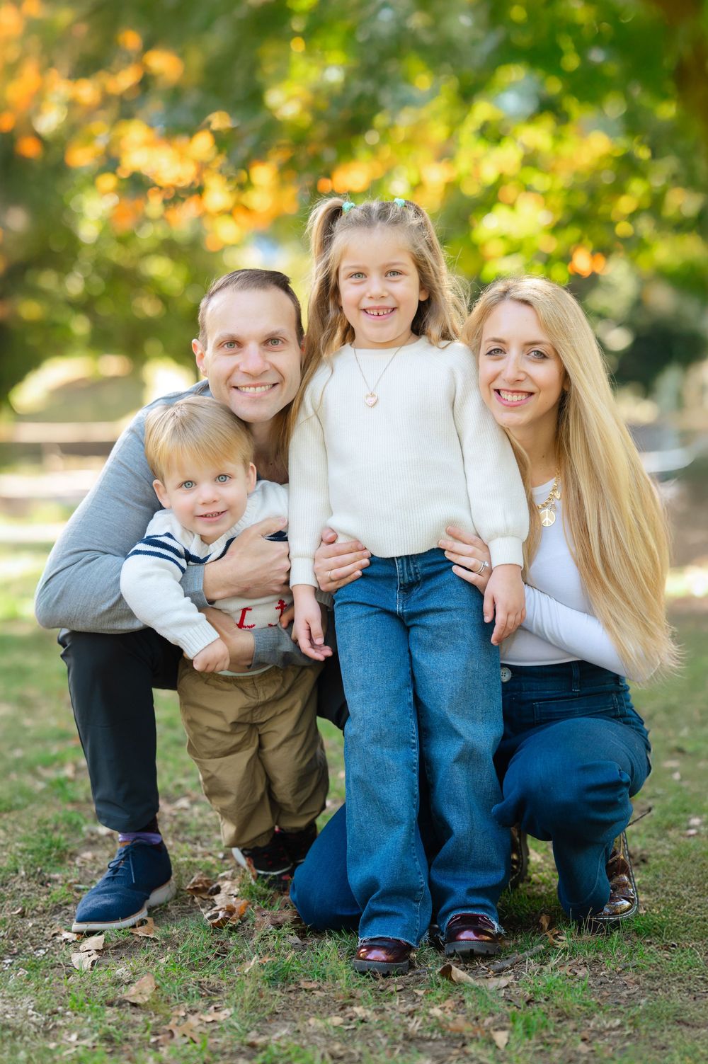 Family sitting together outdoors in autumn with fall foliage and sunlight creating a warm natural setting.