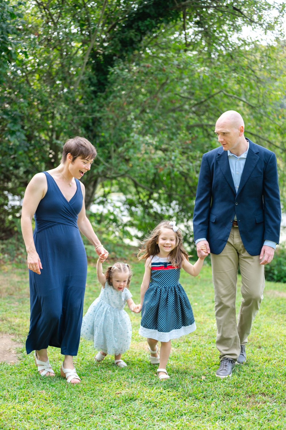 A family walks together holding hands across a grassy lawn in coordinated navy blue and white outfits.