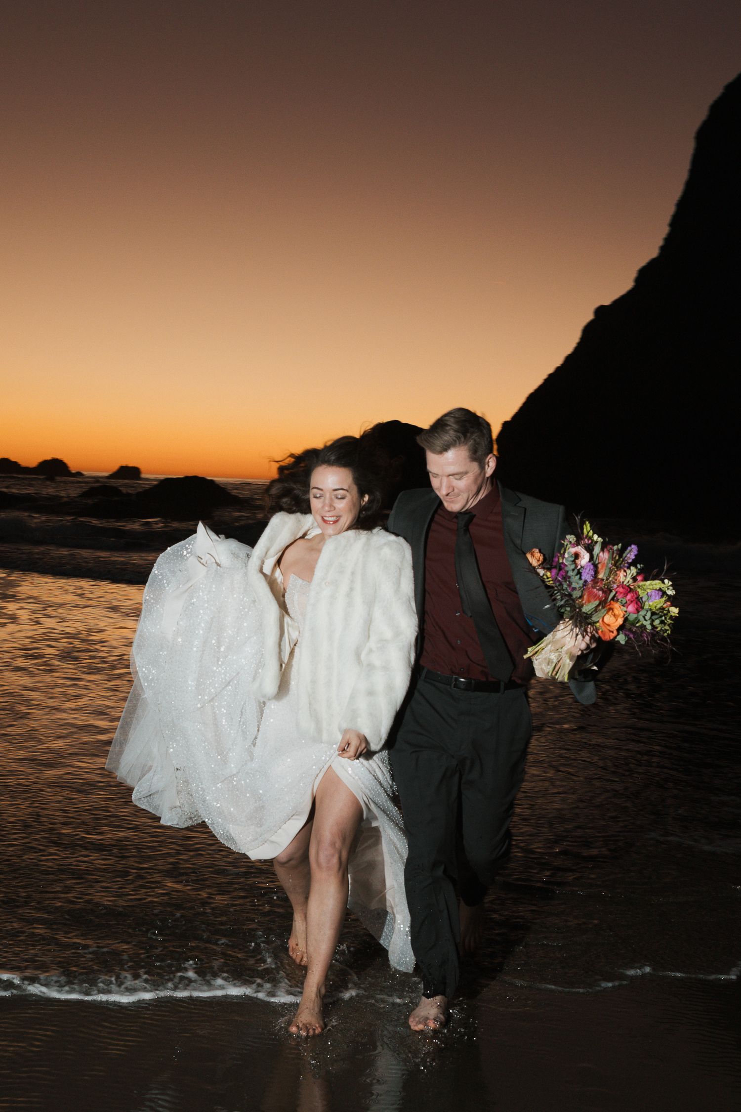 A romantic wedding couple embraces under a flowing white veil against a bright blue sky.