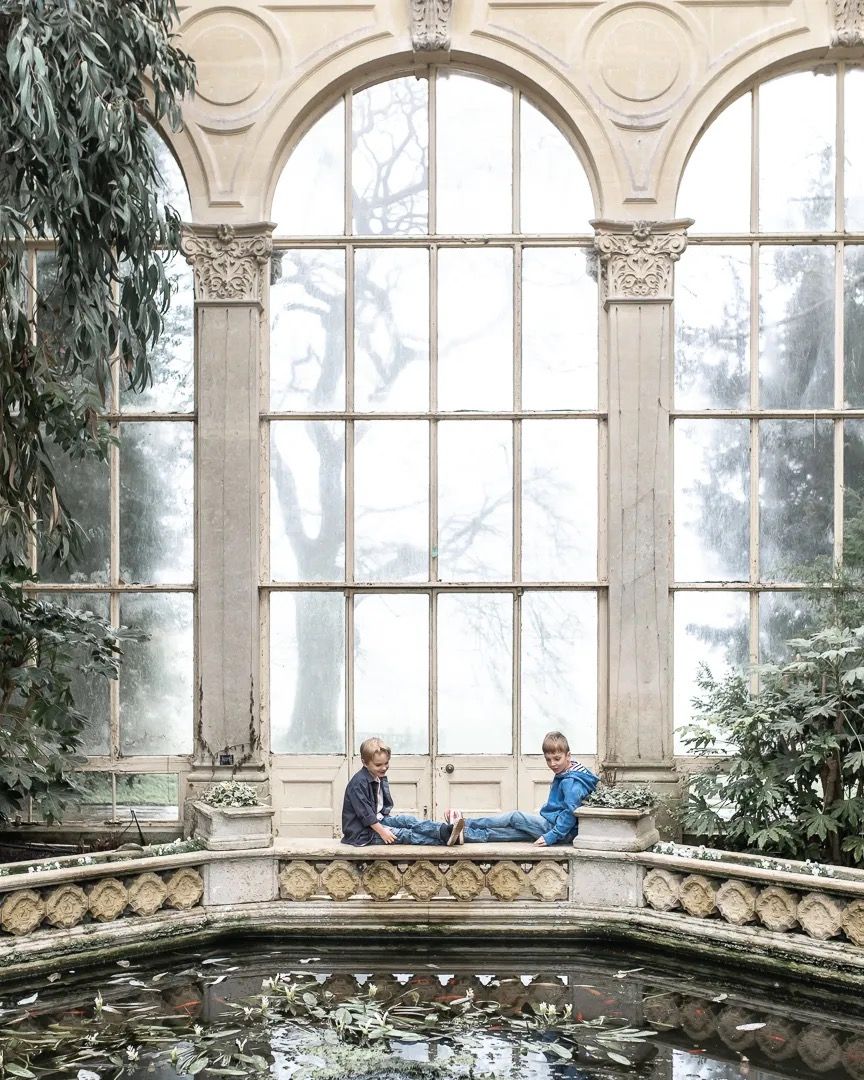 Family sitting beside a large arched window surrounded by indoor greenery.