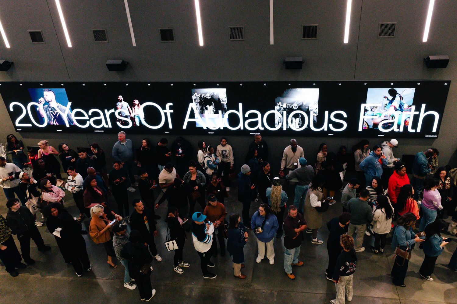 A crowd gathers beneath a large LED sign reading 20 Years Of Audacious Faith at a celebratory event.