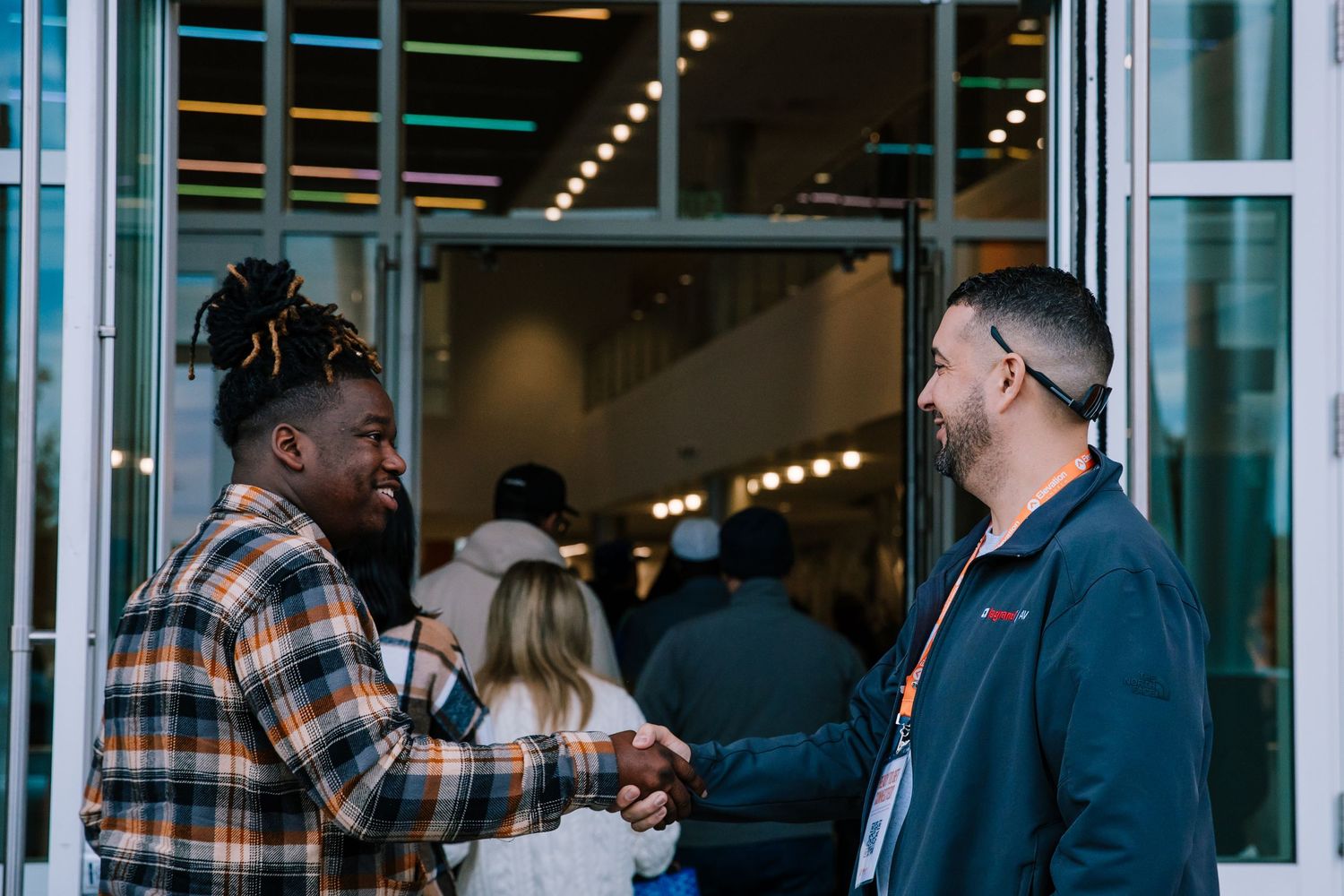 Two men shaking hands and greeting each other outside a modern building entrance.