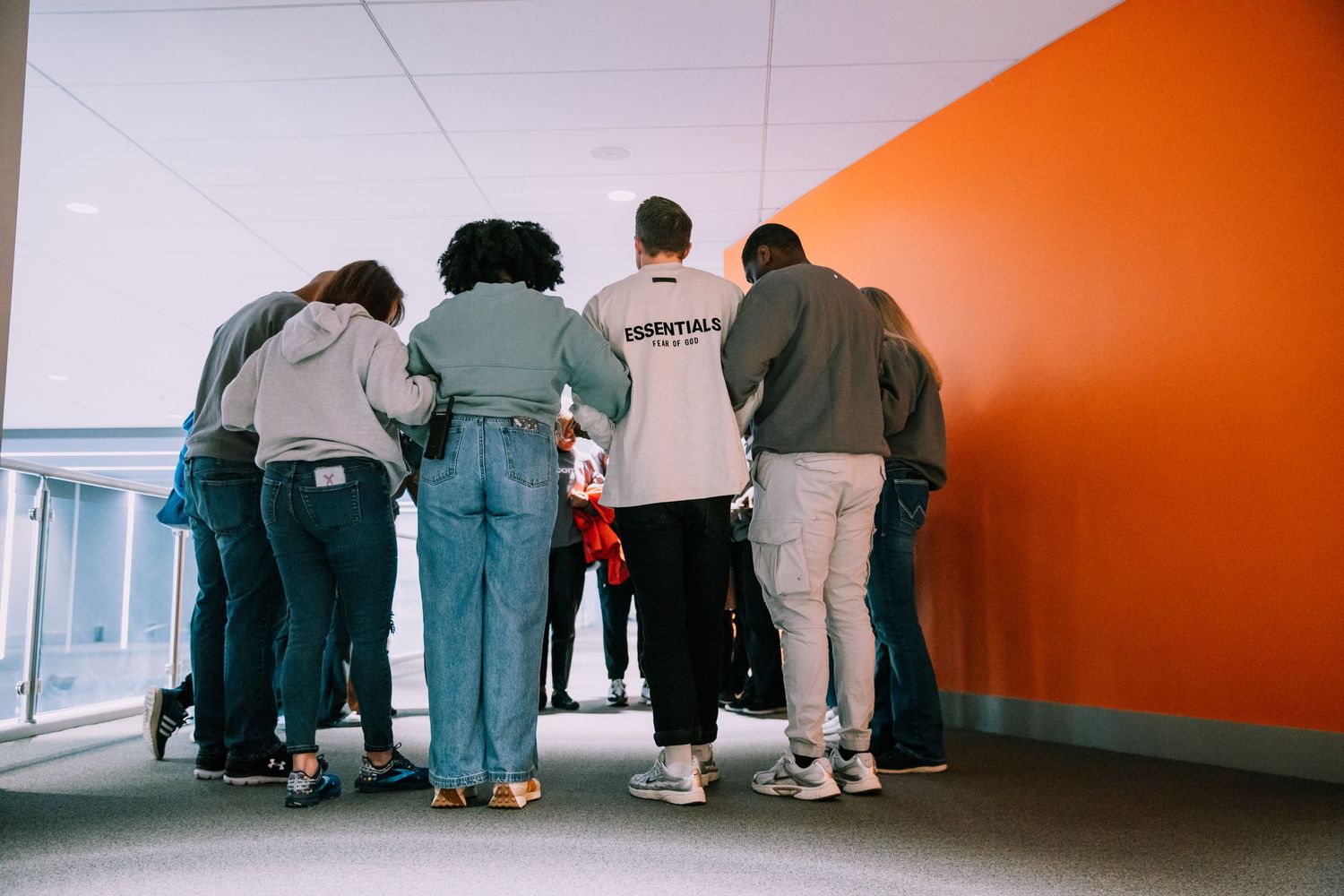 Small group of people huddled together praying in a hallway with an orange wall.