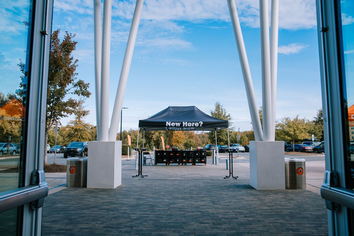 View through glass doors of a outdoor tent with Now Here sign in a parking lot.