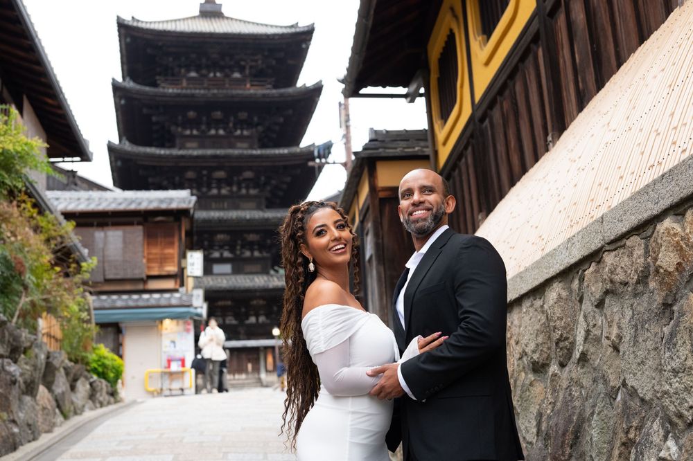 Couple poses smiling in front of a five-story pagoda on a historic cobblestone street in Kyoto, Japan.