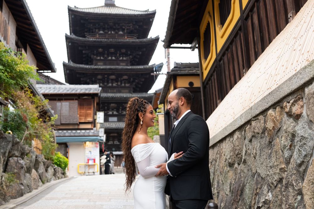 Bride and groom share an intimate moment facing each other near a towering pagoda in Kyoto, Japan.
