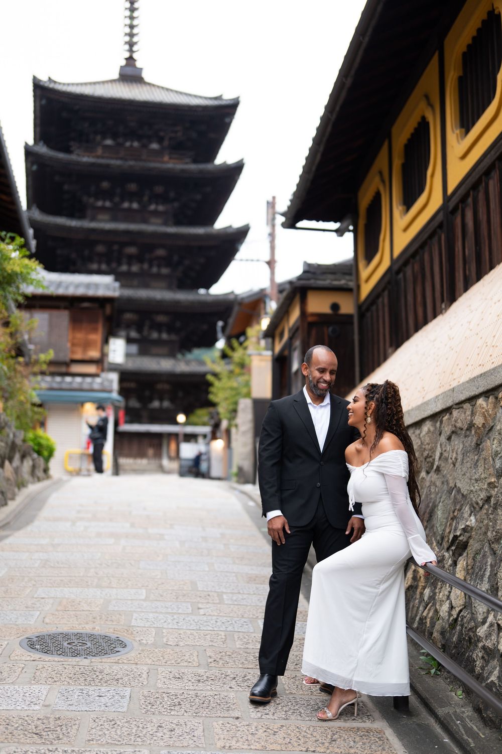 Couple walks and laughs together on a scenic stone-paved path with a five-story pagoda in Kyoto, Japan.