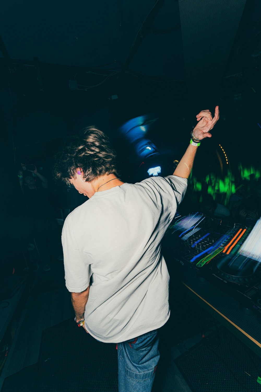 A person in a white t-shirt and jeans dances energetically in a dark nightclub with blue lighting.