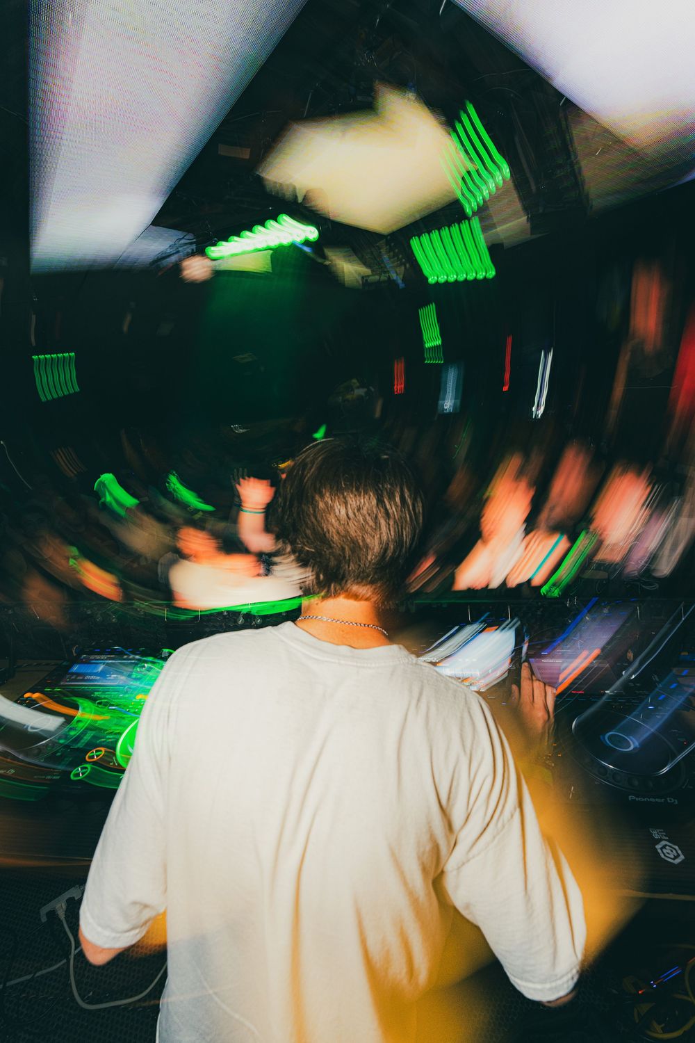 DJ performs at a nightclub with green lighting effects creating a dynamic motion-blur atmosphere.