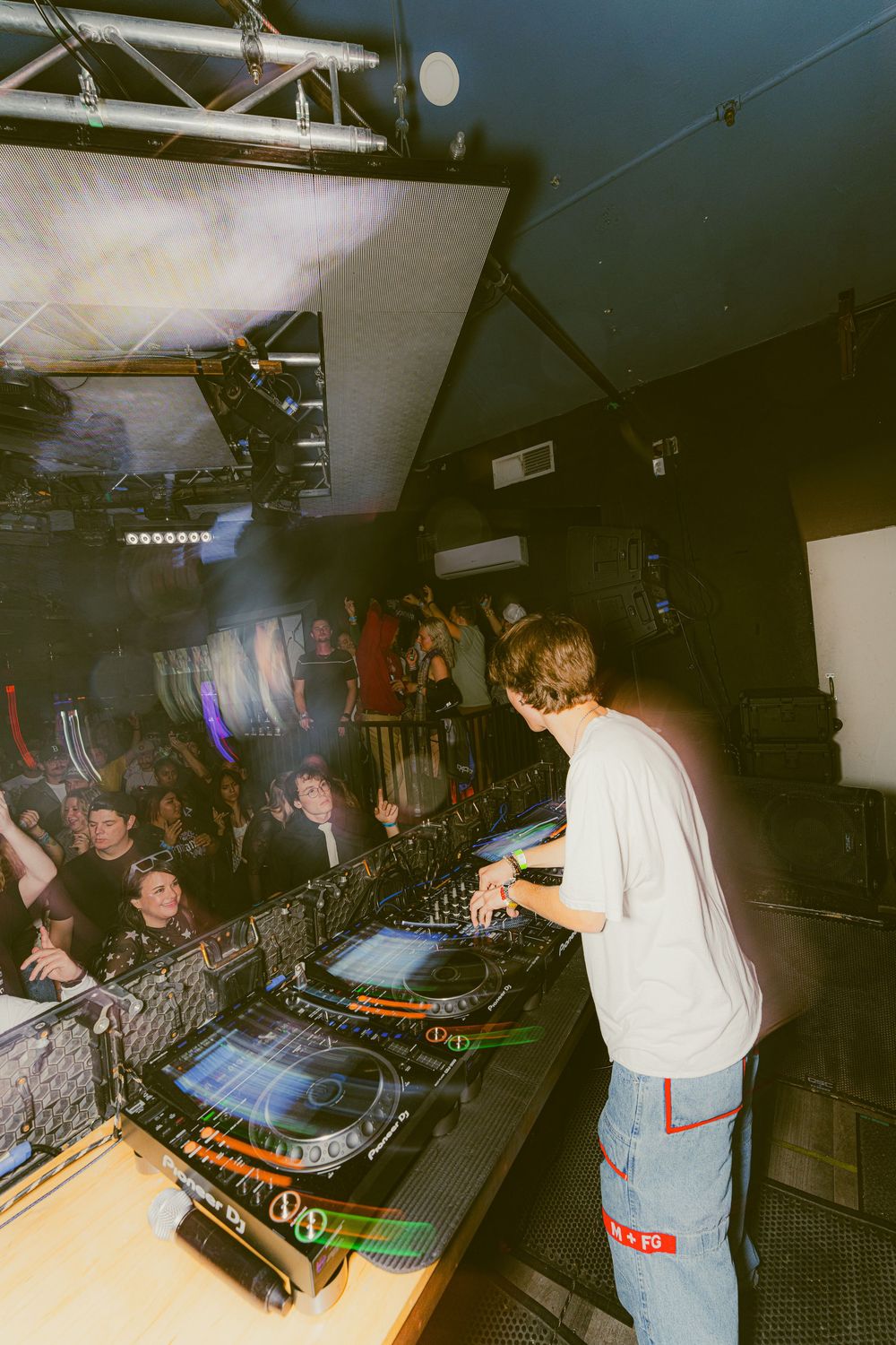 DJ performing at a nightclub with vintage turntables and mixing equipment in a dimly lit environment.