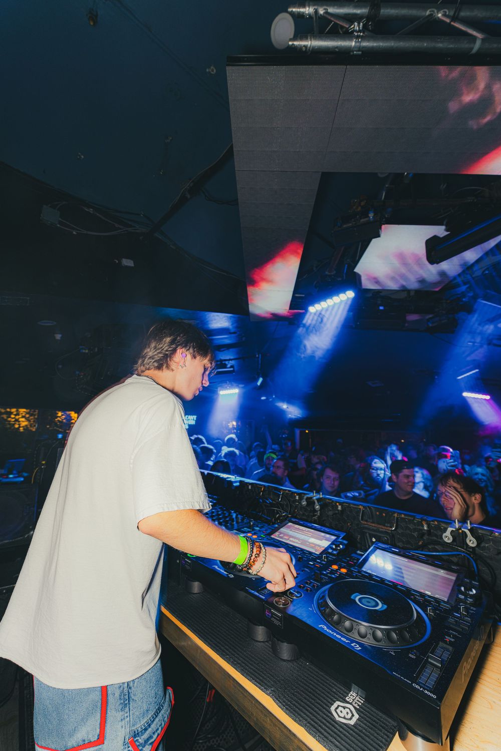 DJ performs at nightclub with professional equipment and blue lighting in dark atmospheric setting.